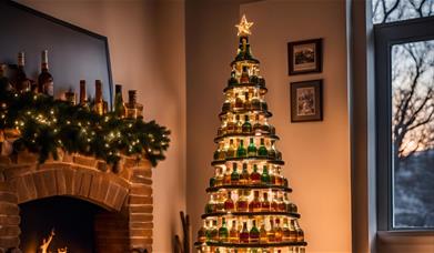 A christmas tree in a cartoon style beside a fireplace and covered in layers of empty whisky bottles.