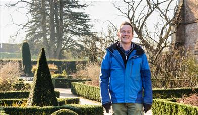 An image of a man wearing a coat and smiling in a garden in winter