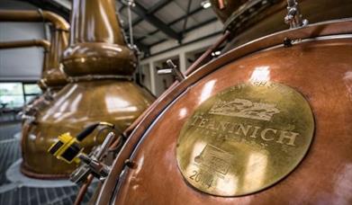 A close up image of the copper jacket of a whisky still. The distilleries name is engraved on the copper coloured hatch for the still. The distillery