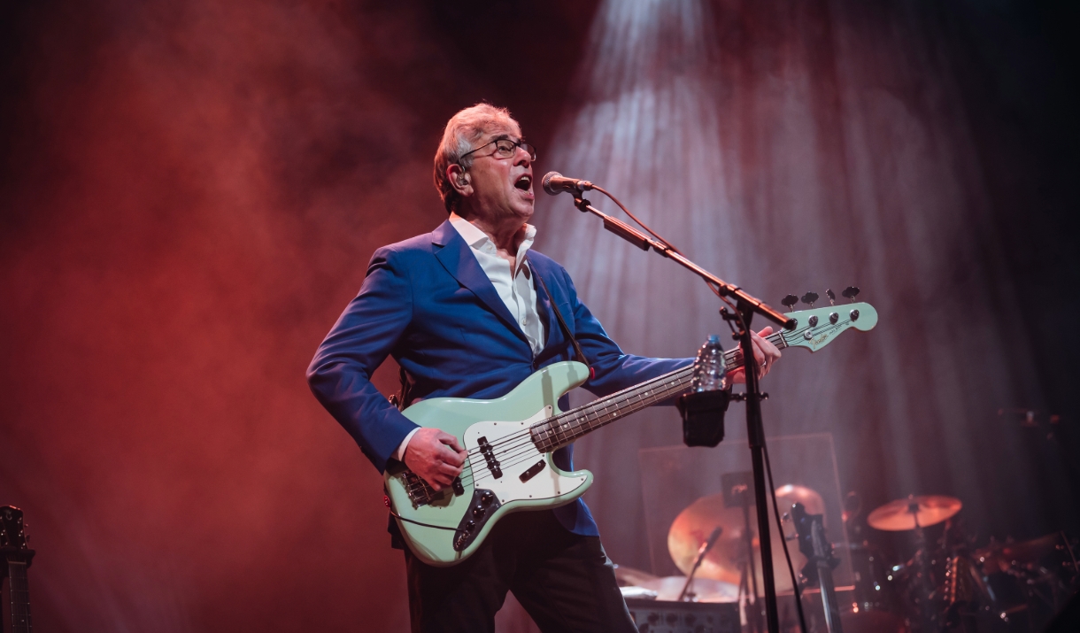 A photo of Graham Gouldman. He is playing an electric guitar while singing