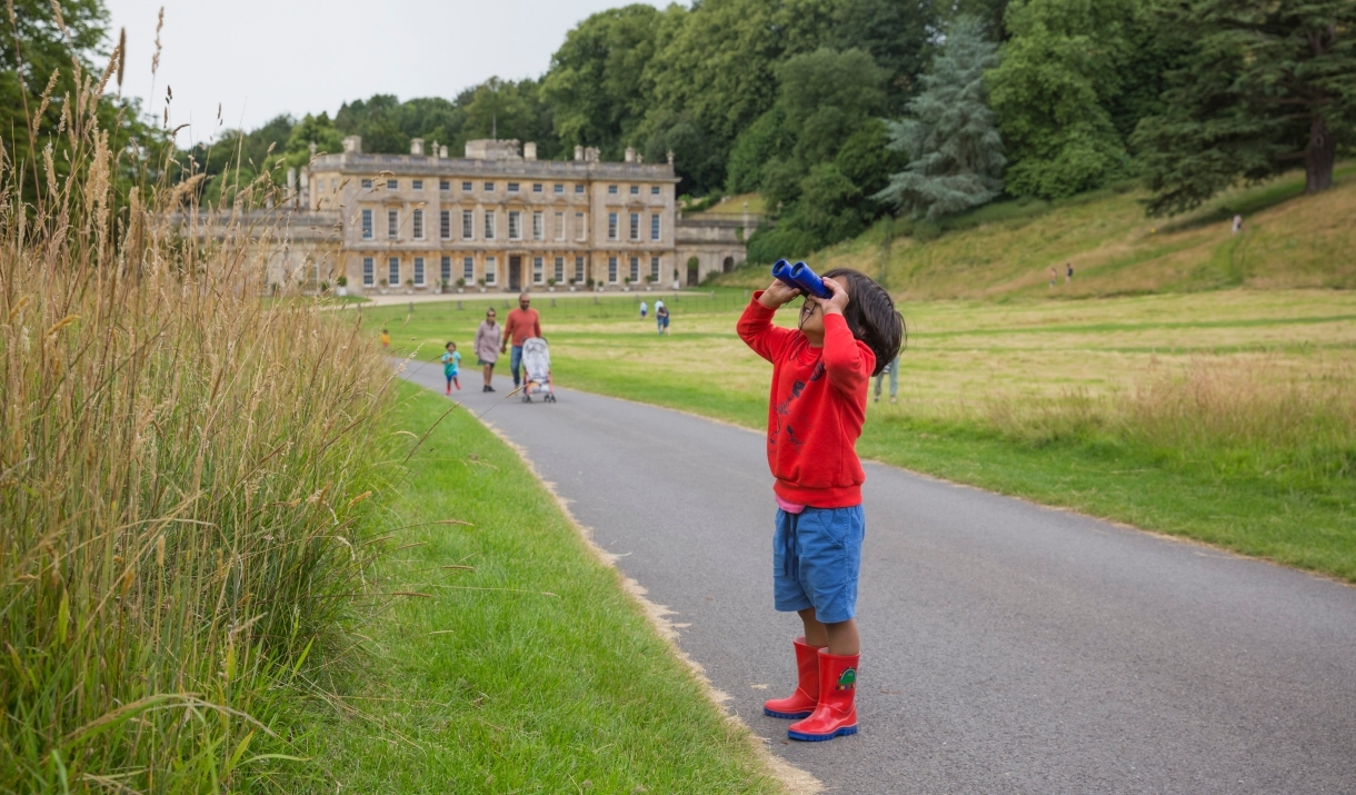 Boy looking through binoculars into parkland in front of a historic house