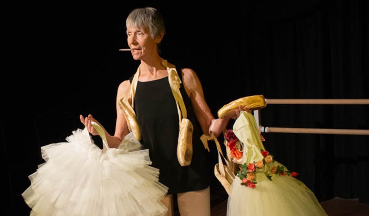 A woman in her 60's holding up ballet uniforms.