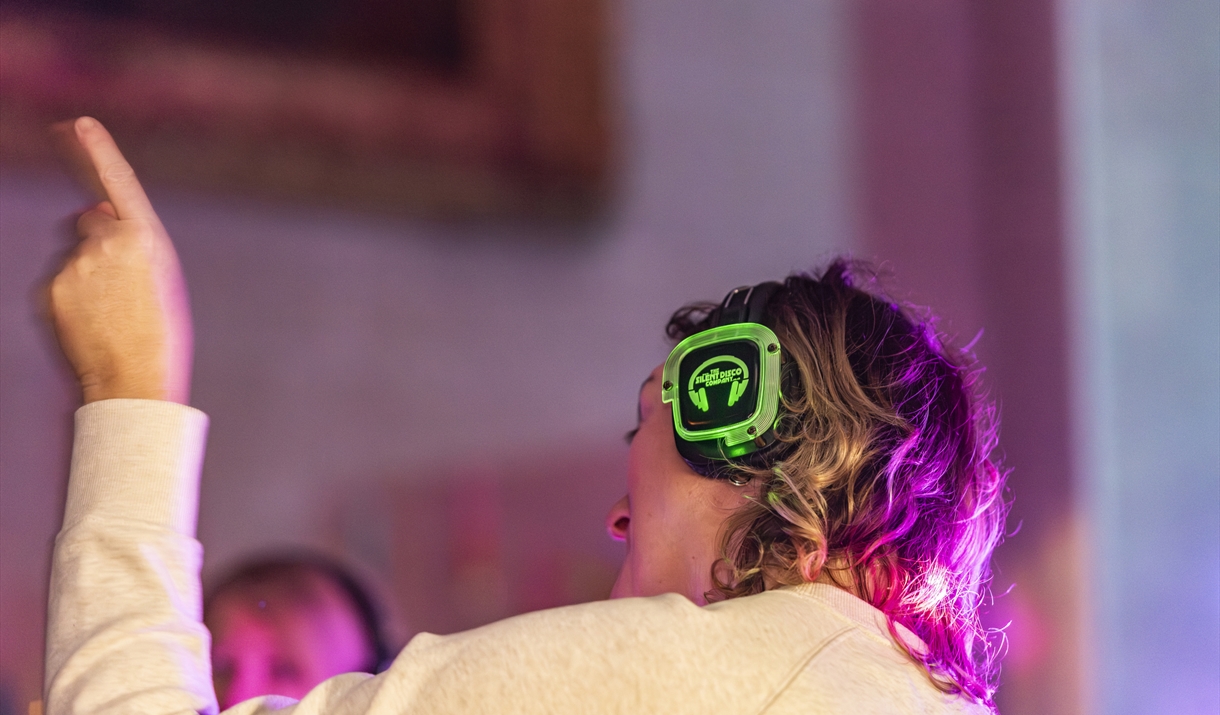 A person wearing a pair of silent disco headphones waving their arm in the air.