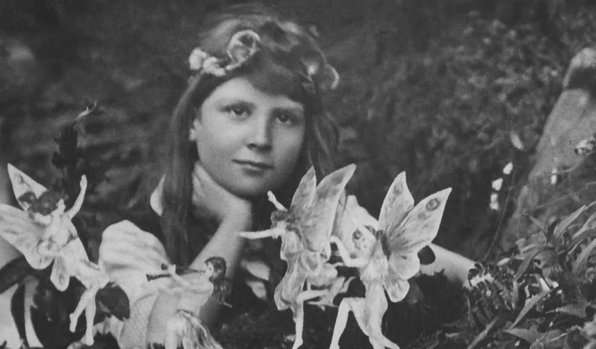 A black and white image of a child with long hair, with miniature fairies dancing around them.