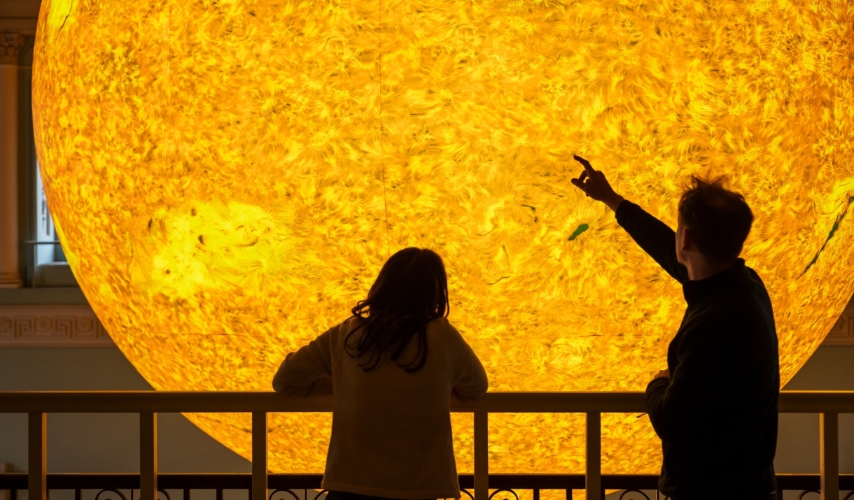 Two people looking closely at Helios at Bath Assembly Rooms