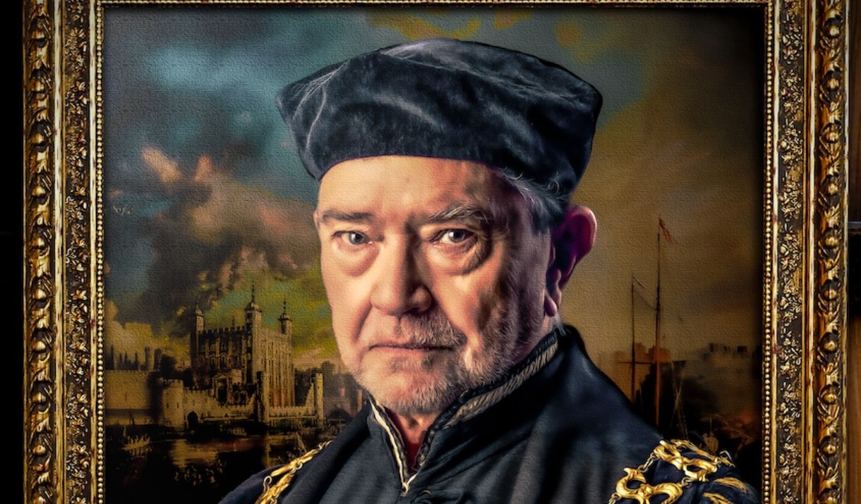 Sir Thomas More stands in front of a painting of that era.