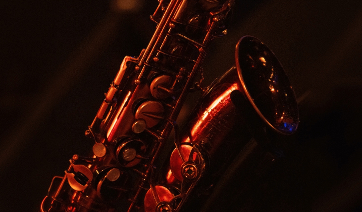 A saxophone bathed in warm red stage lighting against a dark background.