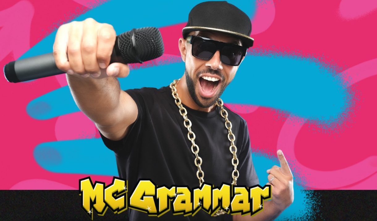 Mc Grammar holding mic toward camera with "MC GRAMMAR" text on a colourful pink and blue background