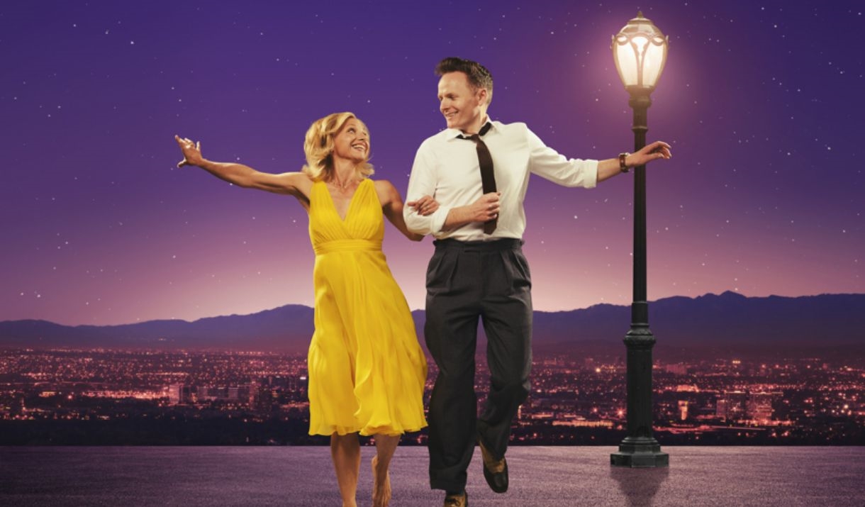 A man and woman, linking arms and jumping, in front a sunset mountain overlooking LA.