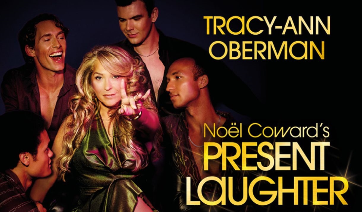 A glamorous woman points at the camera, as 4 young men surround her.