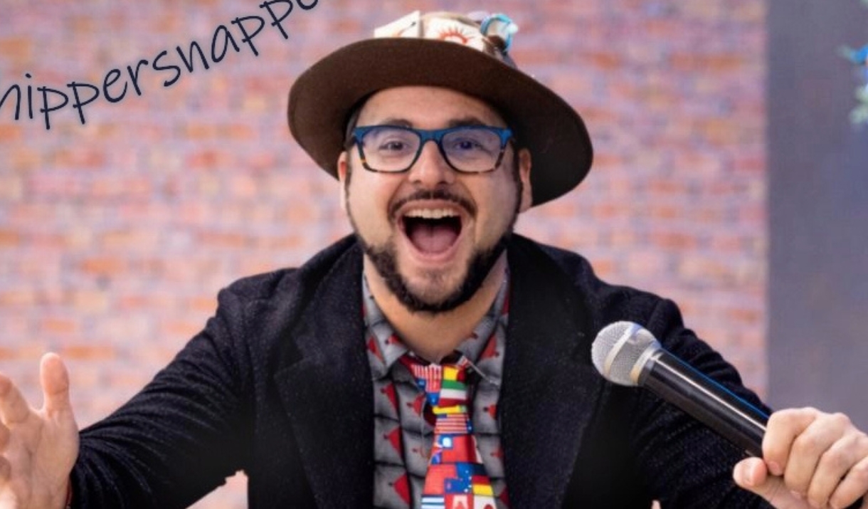 Smiling man in glasses and a hat, holding a microphone
