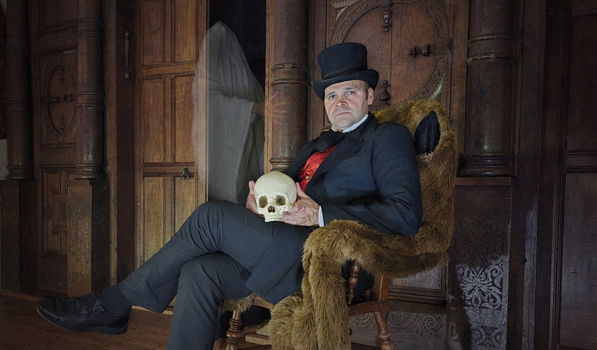 A man in victorian attire with a skull, a ghost is watching him