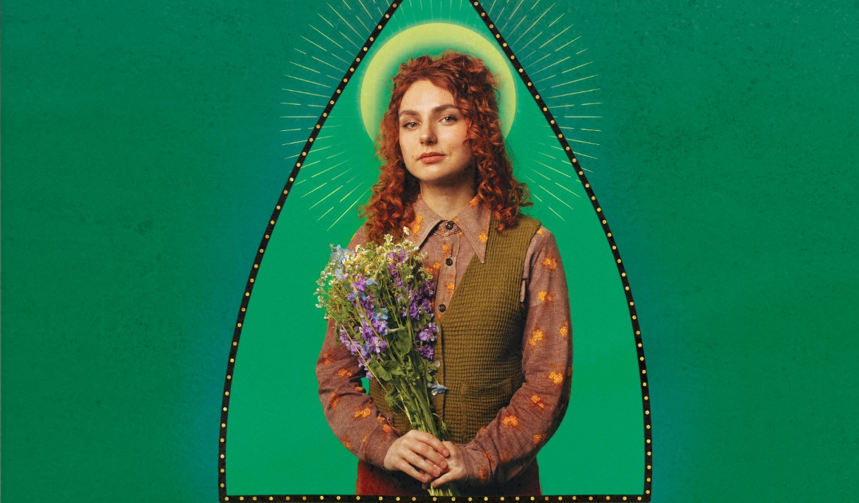 a Image on the comedian Ania Magliano - she is holing a bouquet of flowers against a green background.