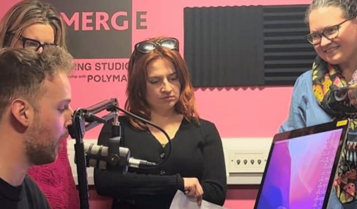 A group huddled around a podcasting set up, engaged in learning. The Polymathic and Emerge logo are at the bottom and the Sparkfest logo is in the top