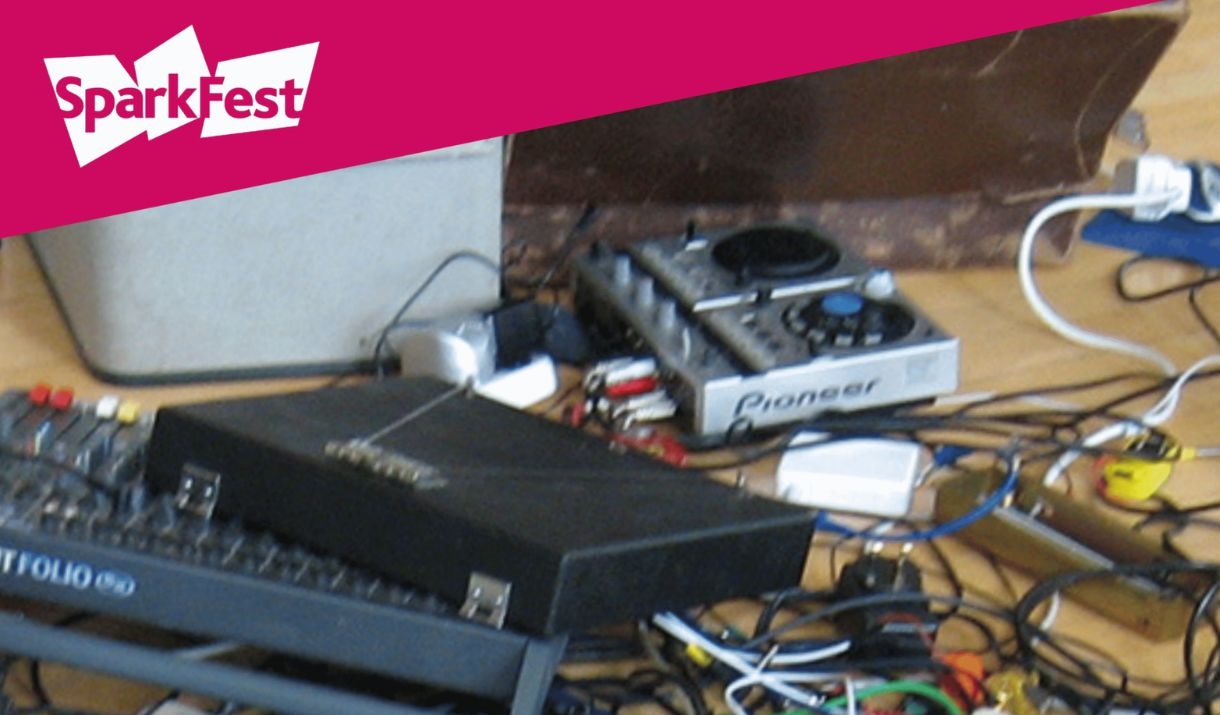 An array of music tech such as pedals and wires sprawled across the floor. Sparkfest logo in top corner