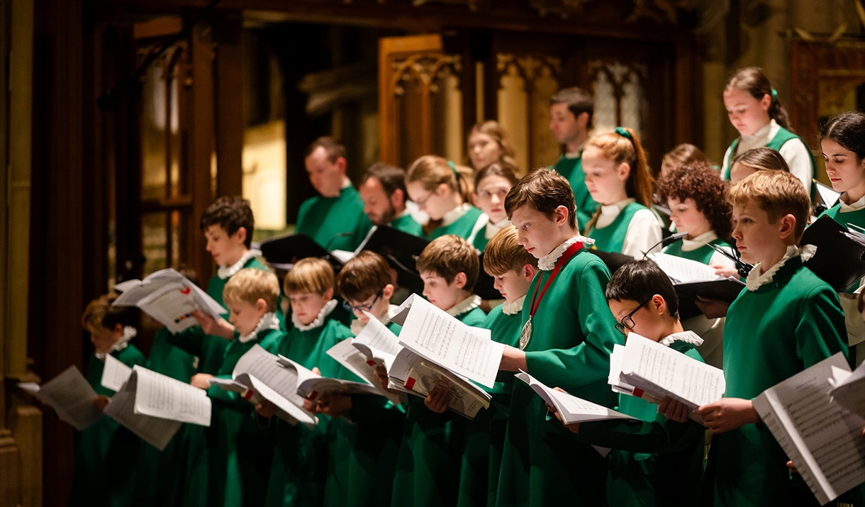 Boys in green choir robes hold sheet music and sing in a church