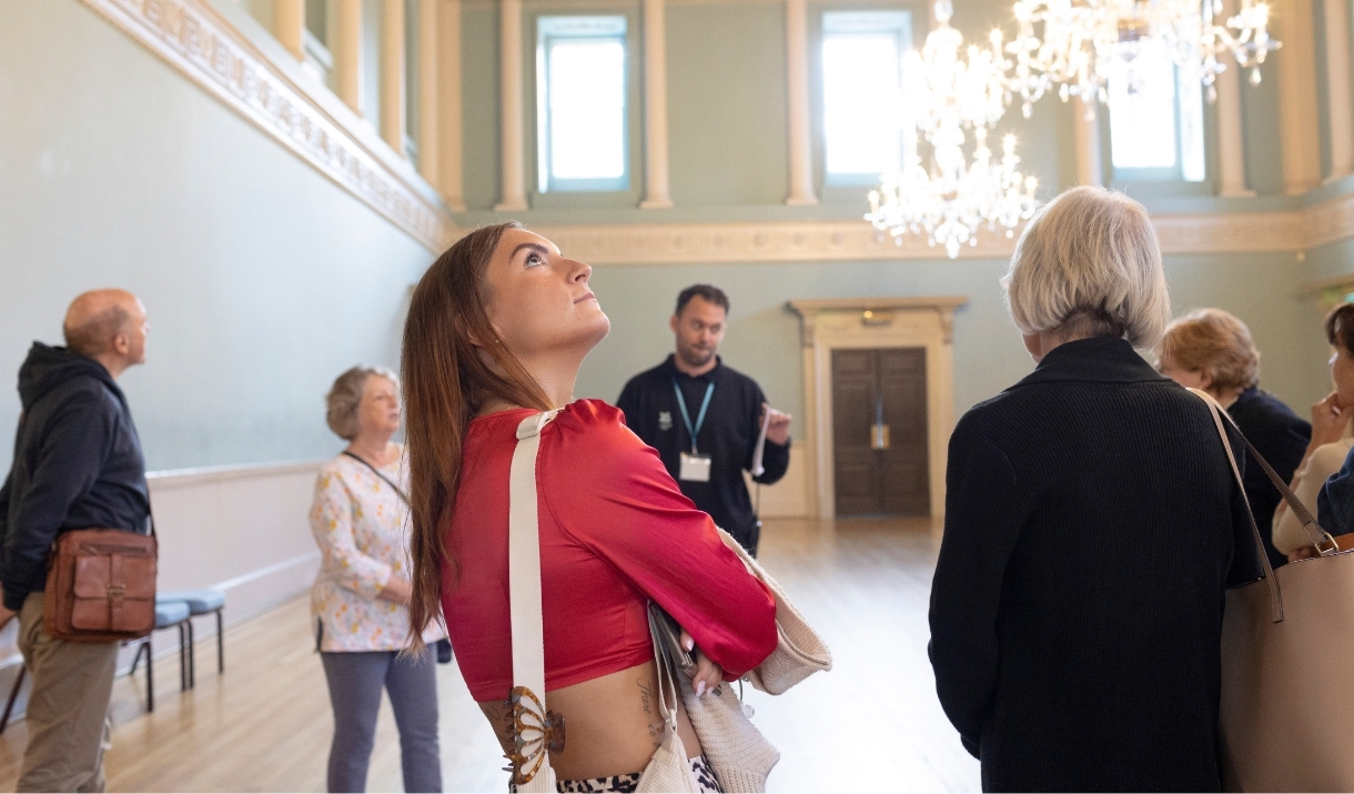 A guided tour group in the Ball Room at Bath Assembly Rooms