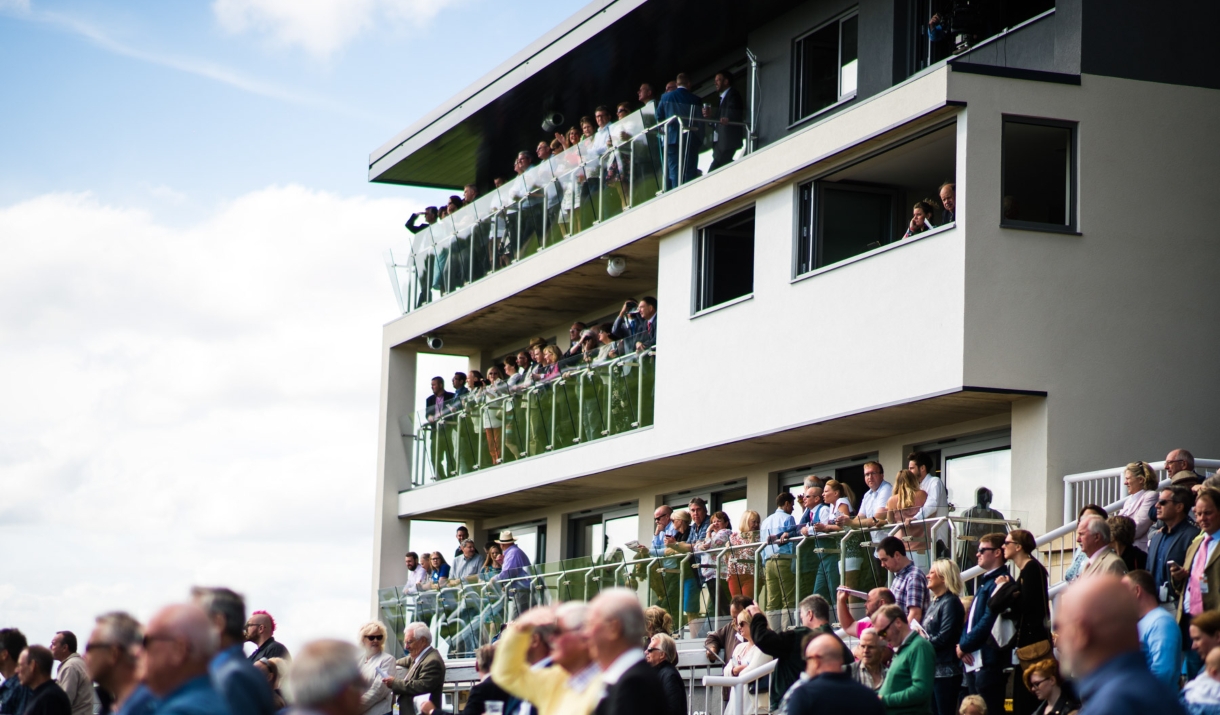 A crowd of spectators watching from the stands at Bath Racecourse