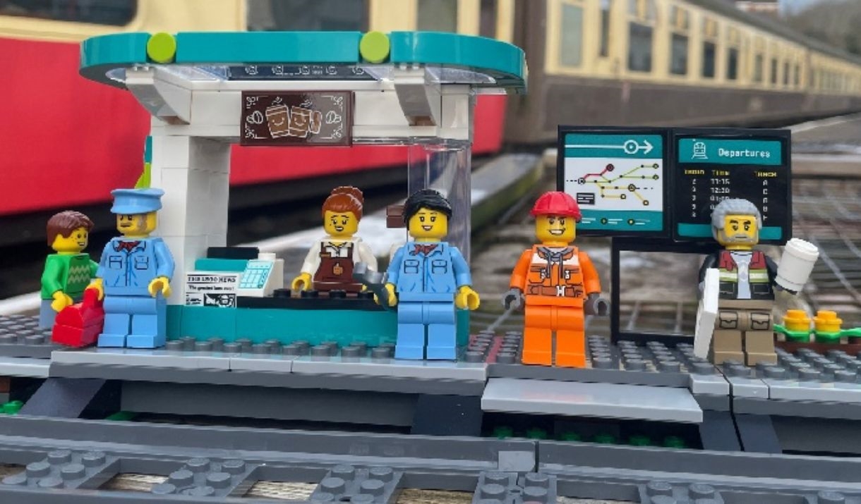 A photograph of some lego figures waiting at a lego railway station.