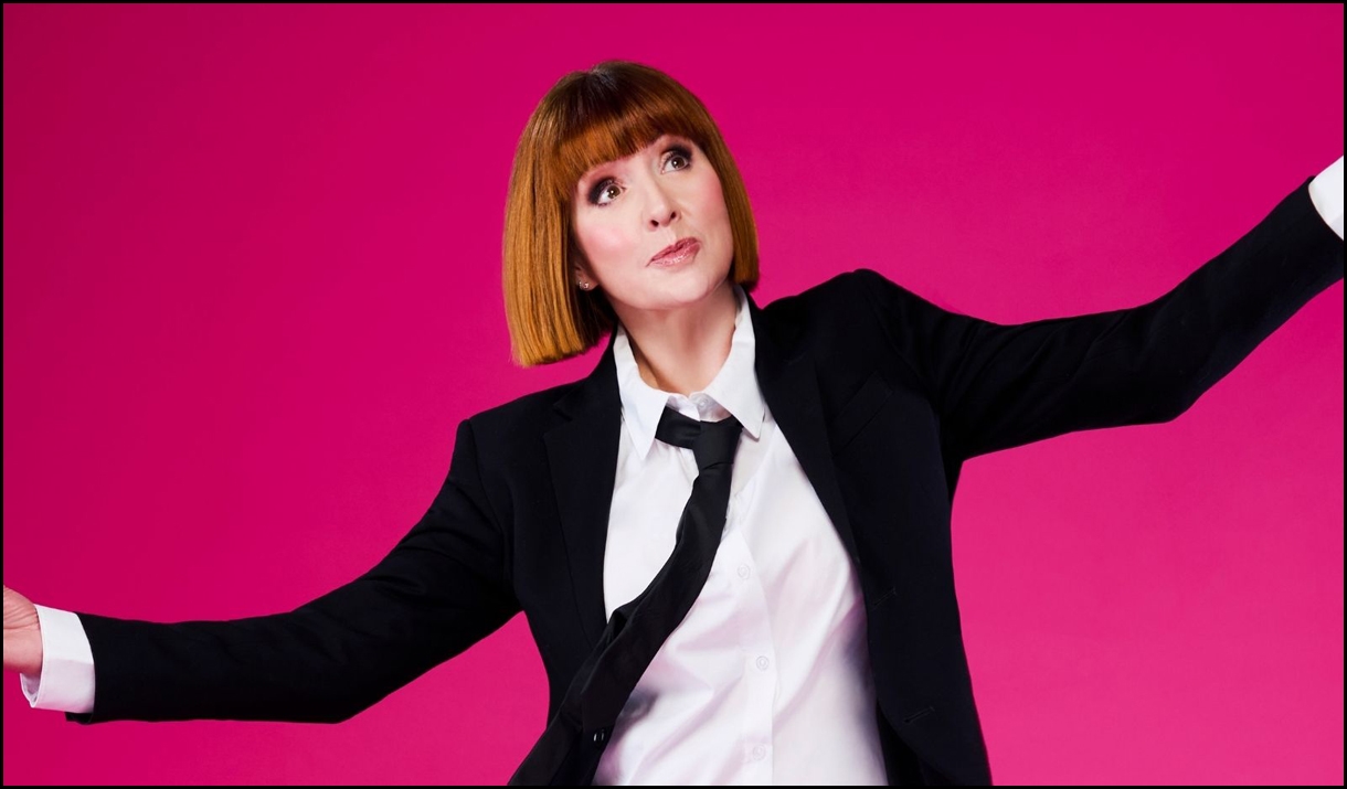 Cally Beaton posing for a picture in a suit, with a bright pink background