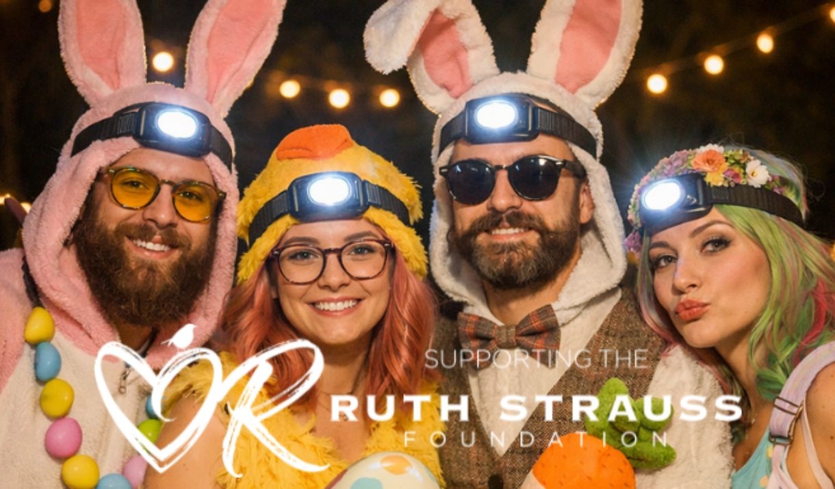 "Four adults wearing Easter-themed costumes including bunny ears and a chick outfit with head torches, smiling at the camera. Text reads 'Supporting t