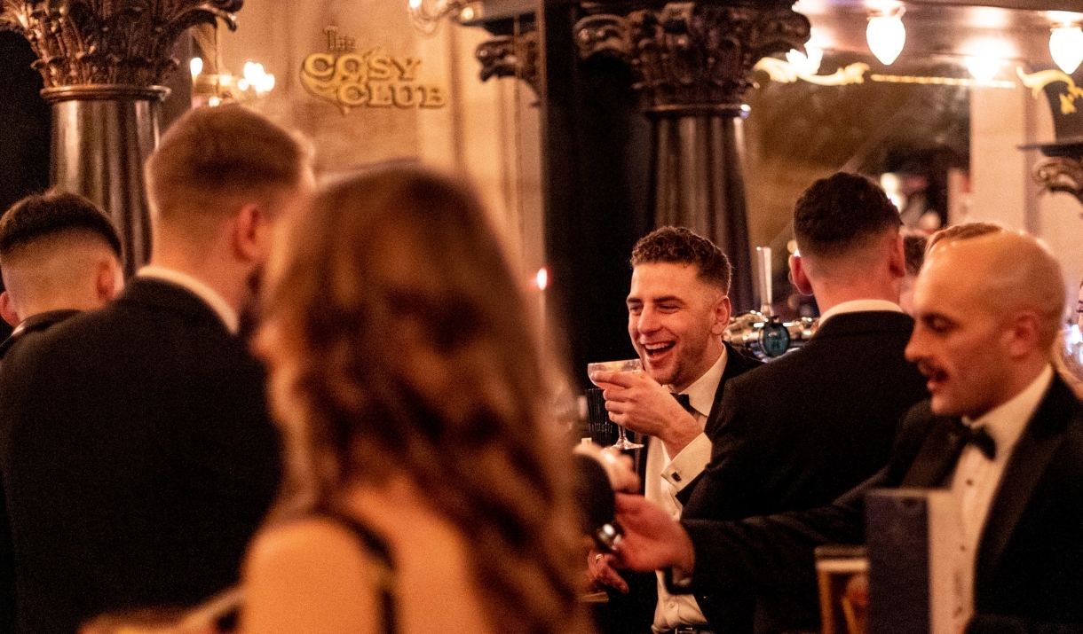 A group of people dressed in black tie attire drinking cocktails in one of Cosy Club's venues.