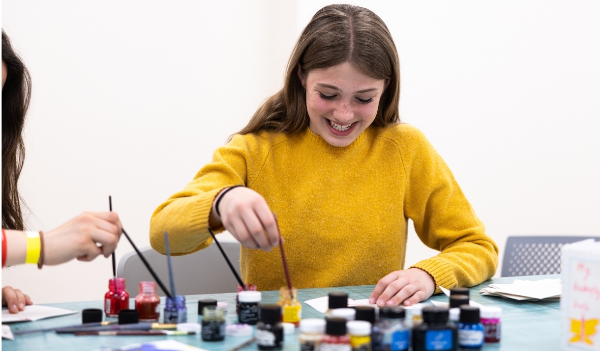 A girl wearing a bright yellow jumper creating an artwork with coloured inks