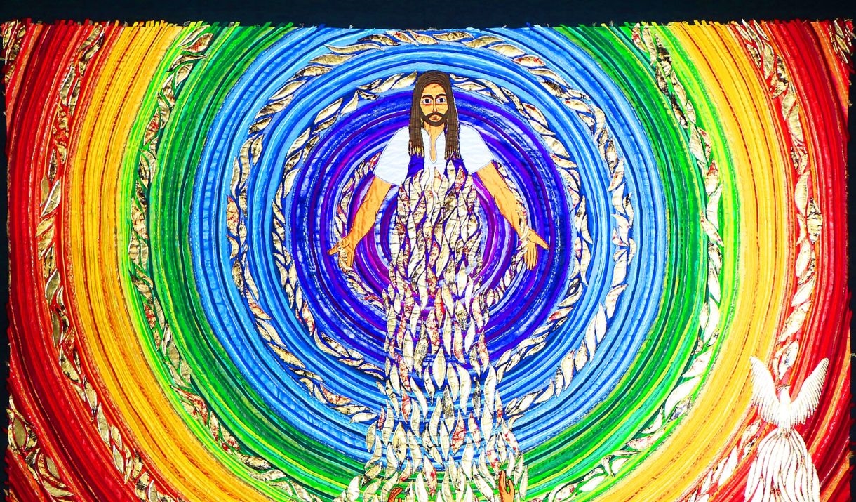 A brightly coloured embroidered panel of Jesus, surrounded by concentric circles of rainbow colours, with a crowd of people in front of Him