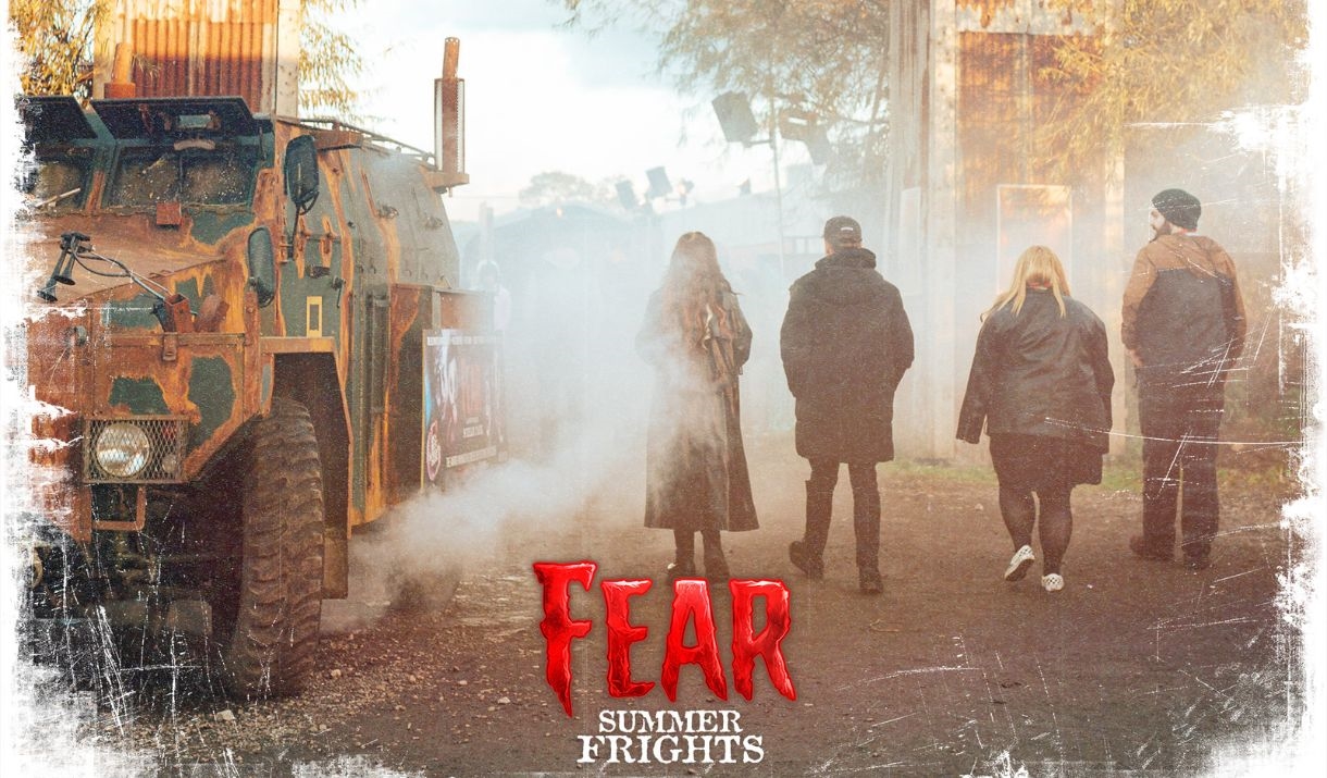 Visitors walking through a foggy, eerie entrance at Fear Summer Frights, featuring an old, rusted military vehicle and industrial structures in the ba