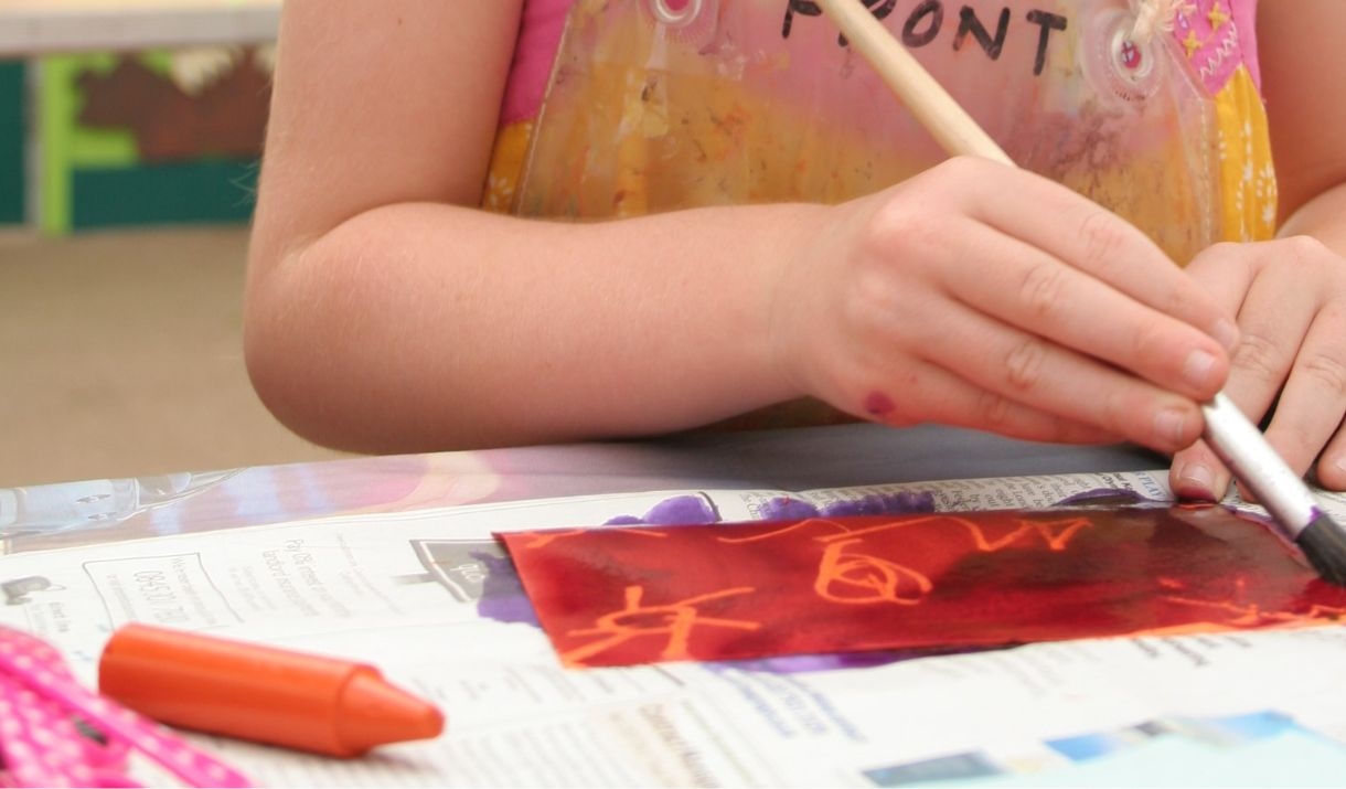 child's hand holding paint brush painting red onto white paper