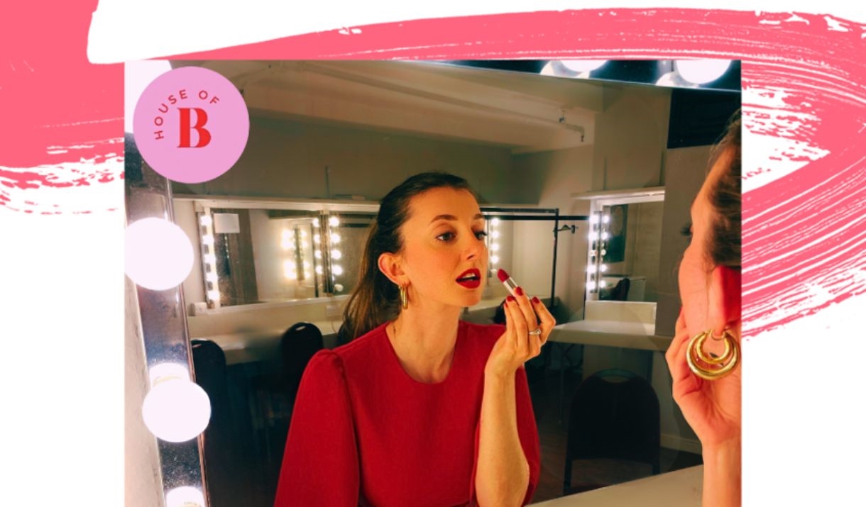 A woman doing her makeup in a dressing room.