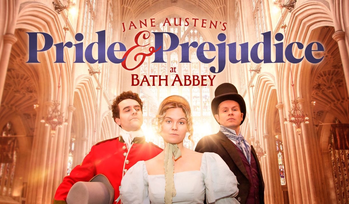 THREE PEOPLE IN A ROW, A WOMEN IN THE MIDDLE OF TWO MEN, ALL WITH A CHEEKY GRIN, LOOKING DOWN THE CAMERA