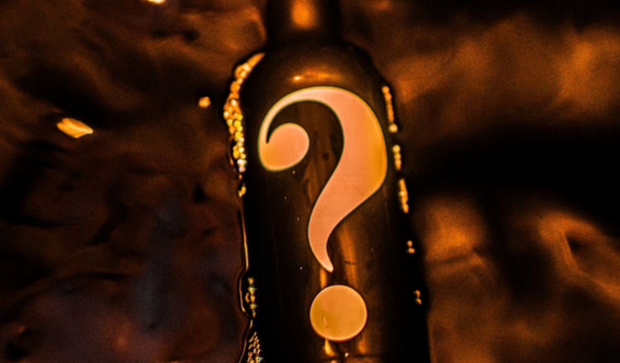 A black whisky bottle with a question mark on it. The background is also dark with smoke and embers of fire floating around the bottle.