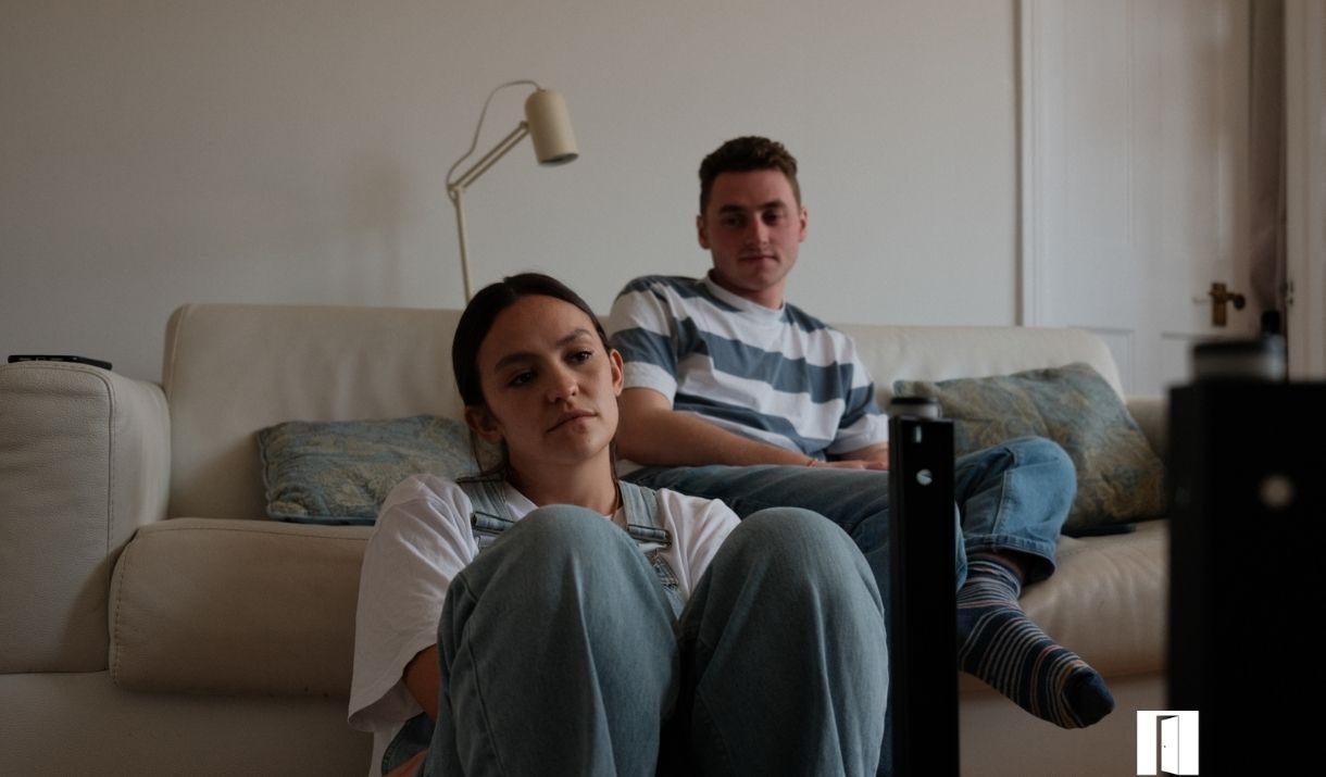 Two people. The male is sitting on a sofa and the female in front of him on the floor.