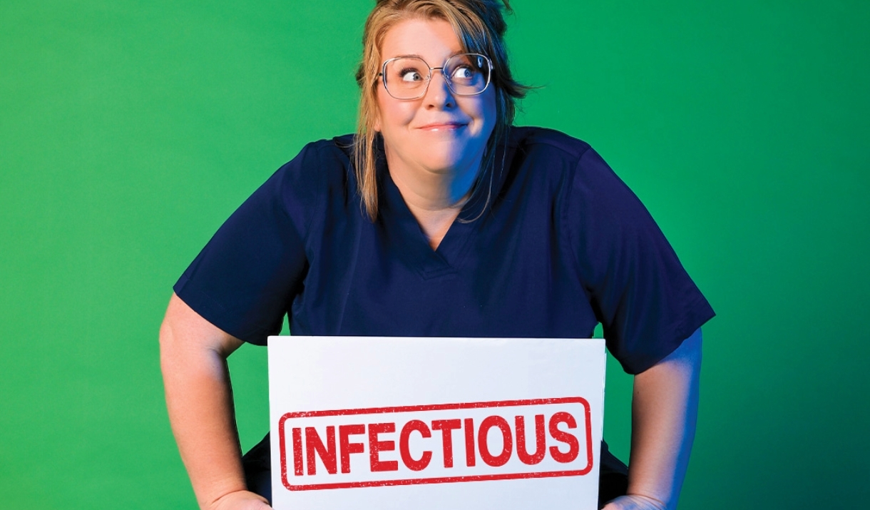 A woman wearing dark hospital scrubs holding a sign that says "infectious" against a green background
