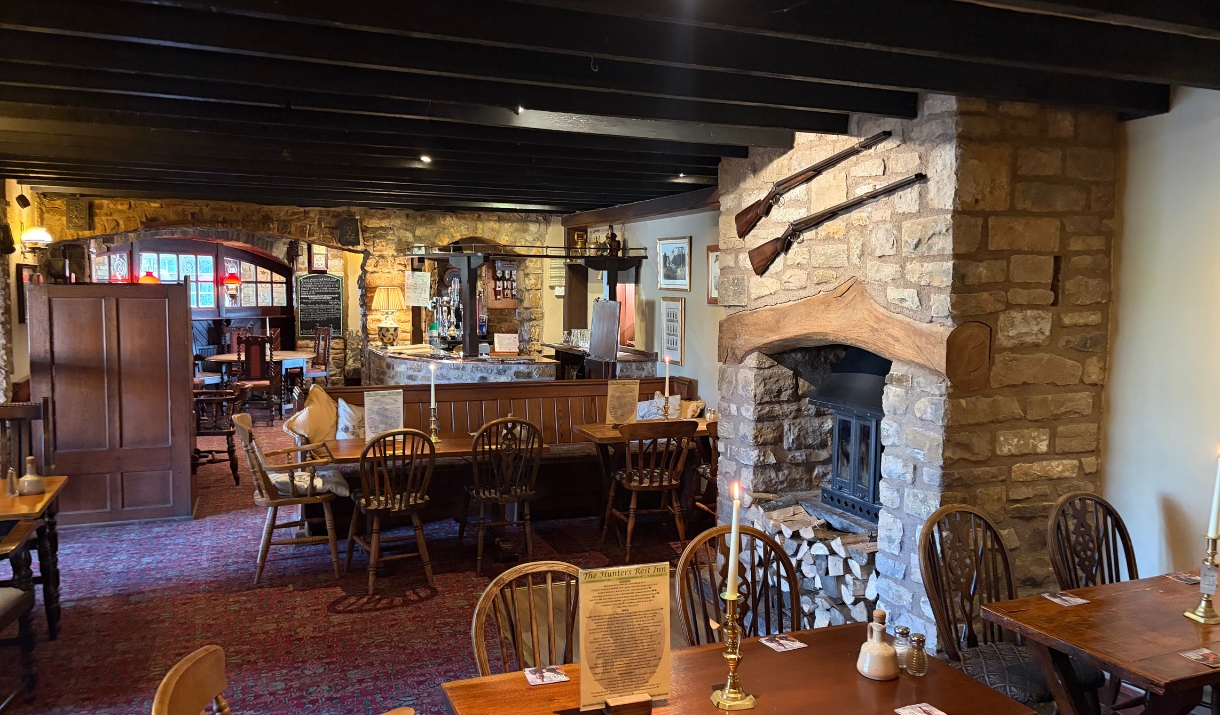 Dining room of pub with stone brick walls and fireplace and wooden tables and chairs.