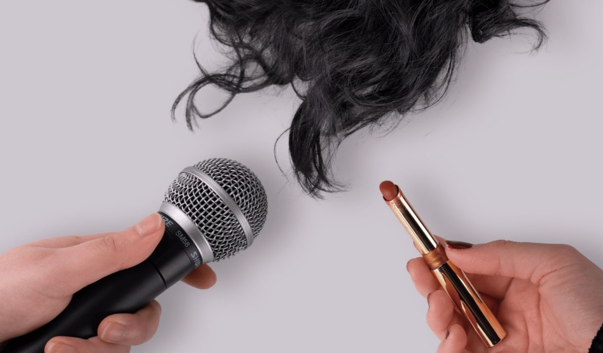 A Black long wig, a microphone, a pair of circular sun glasses, and makeup are each being held out by individual hands. Sparkfest logo in top corner