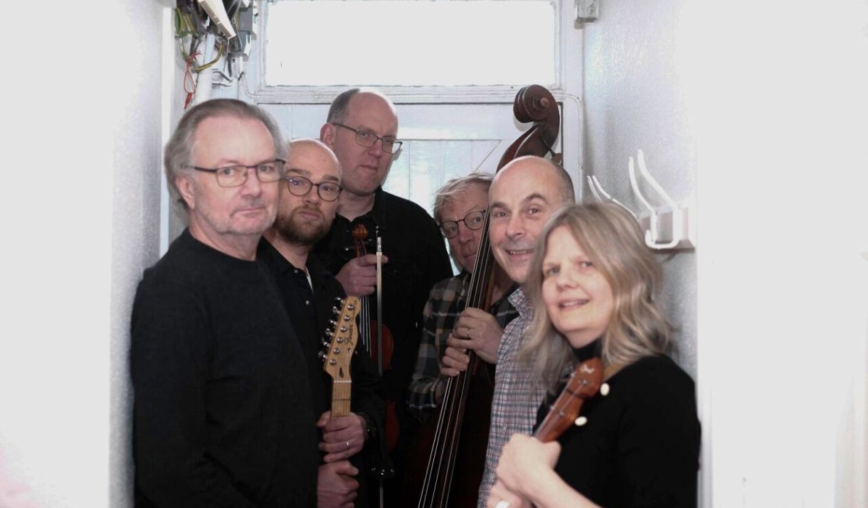 6 people stand in a white small corridor holding string instruments
