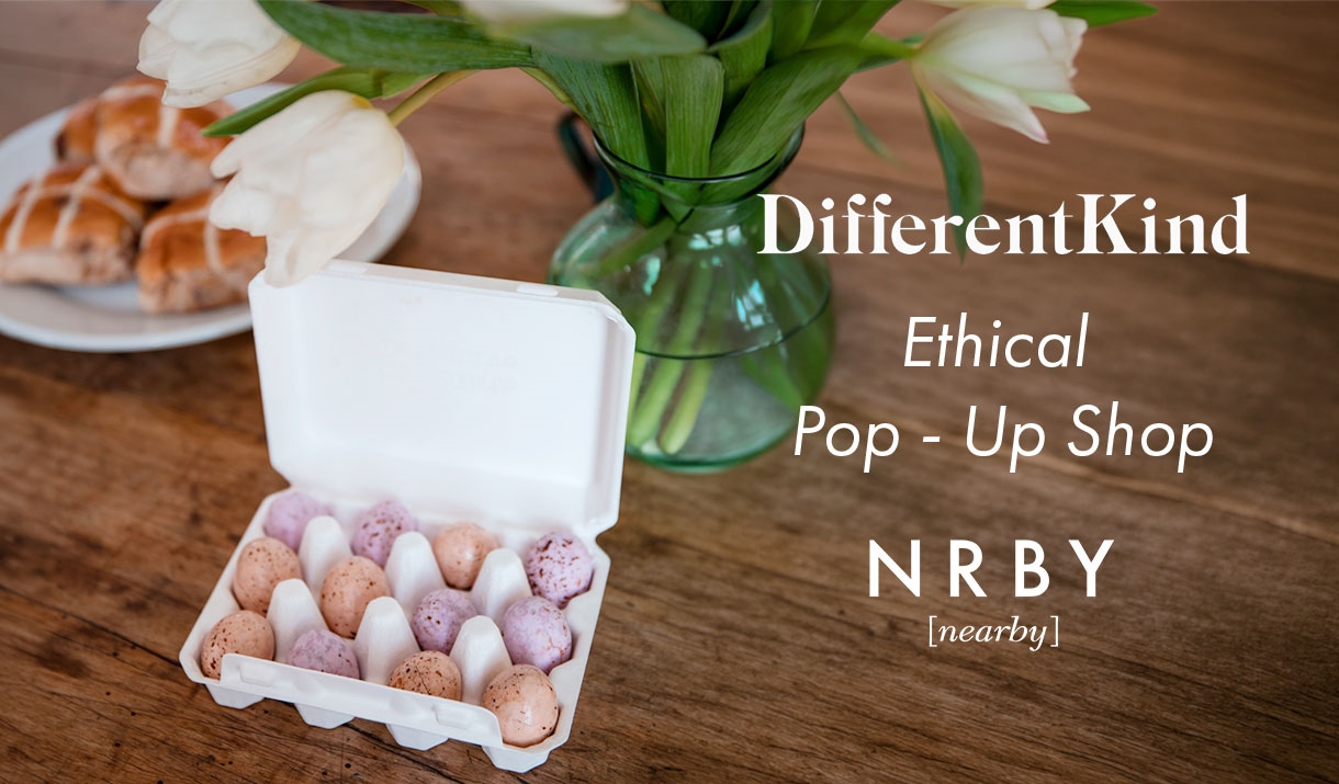 Carton of chocolate eggs in front of a vase of white tulips and plate of hot cross buns. On the right hand side there is white text which reads: Diffe