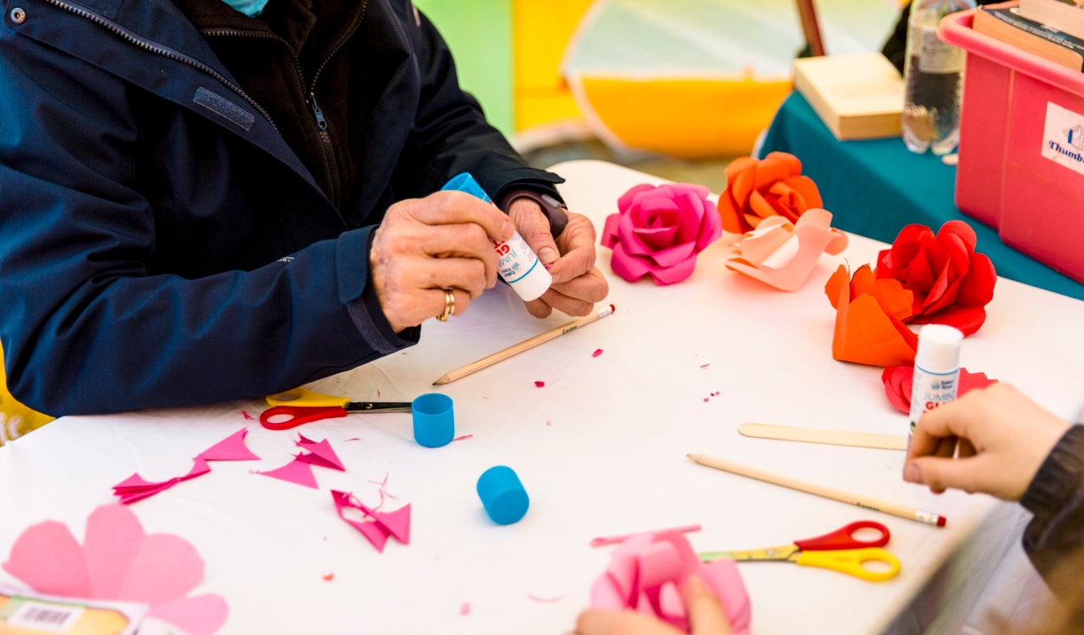 A crafting table with scissors, pencils and paper roses on.
