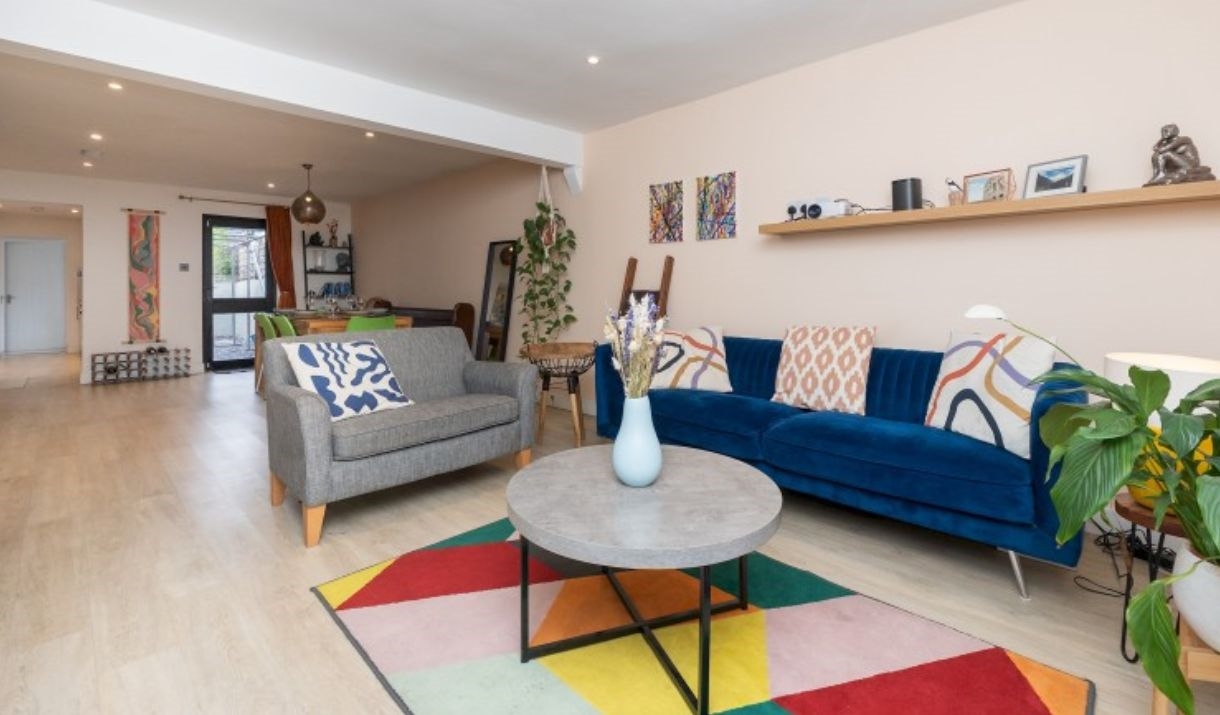 An open-planned living room space with a blue sofa, grey love seat, round coffee table and geometric multi-coloured rug.