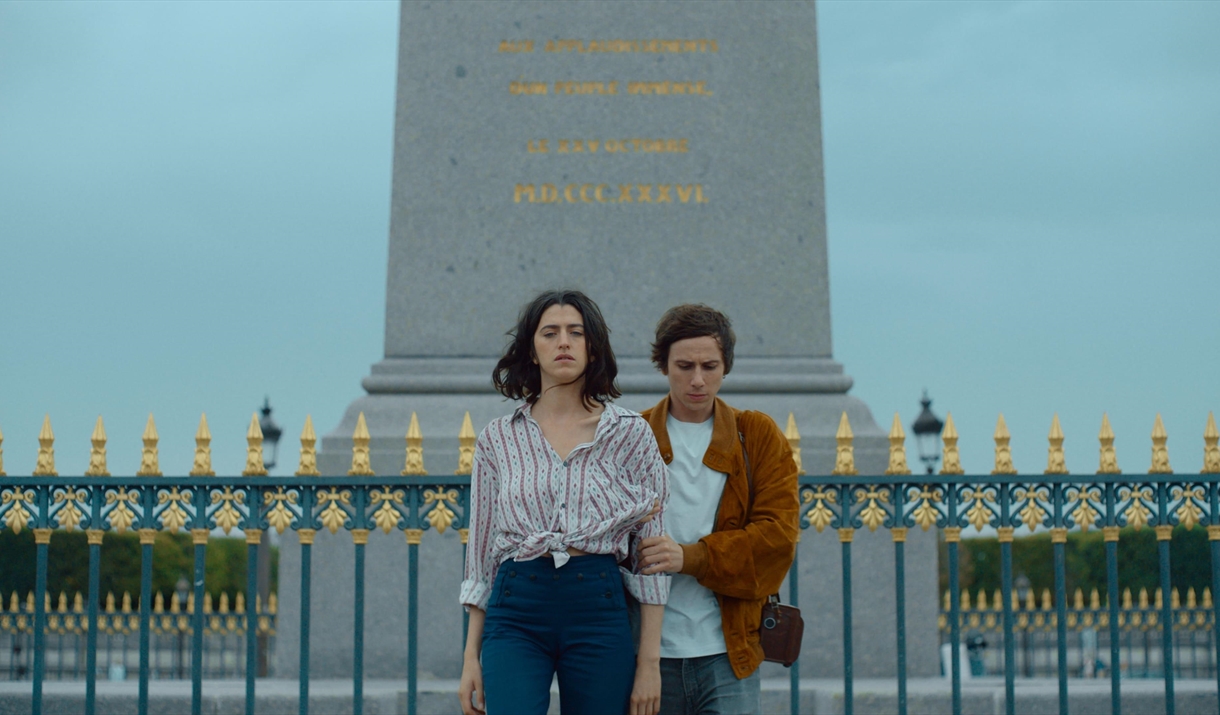 A young man and woman stand looking at the floor.