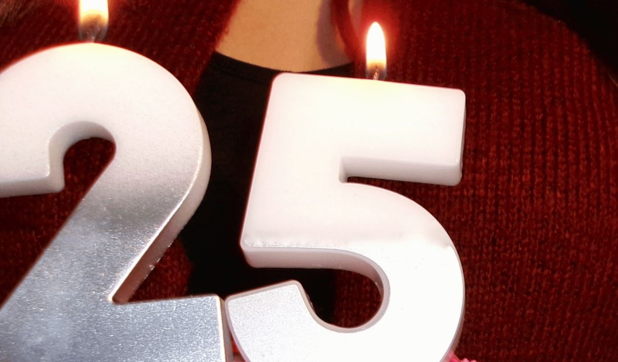 A Birthday cake with candles in the shape of the number 2 and 5. Sparkfest logo in top corner.