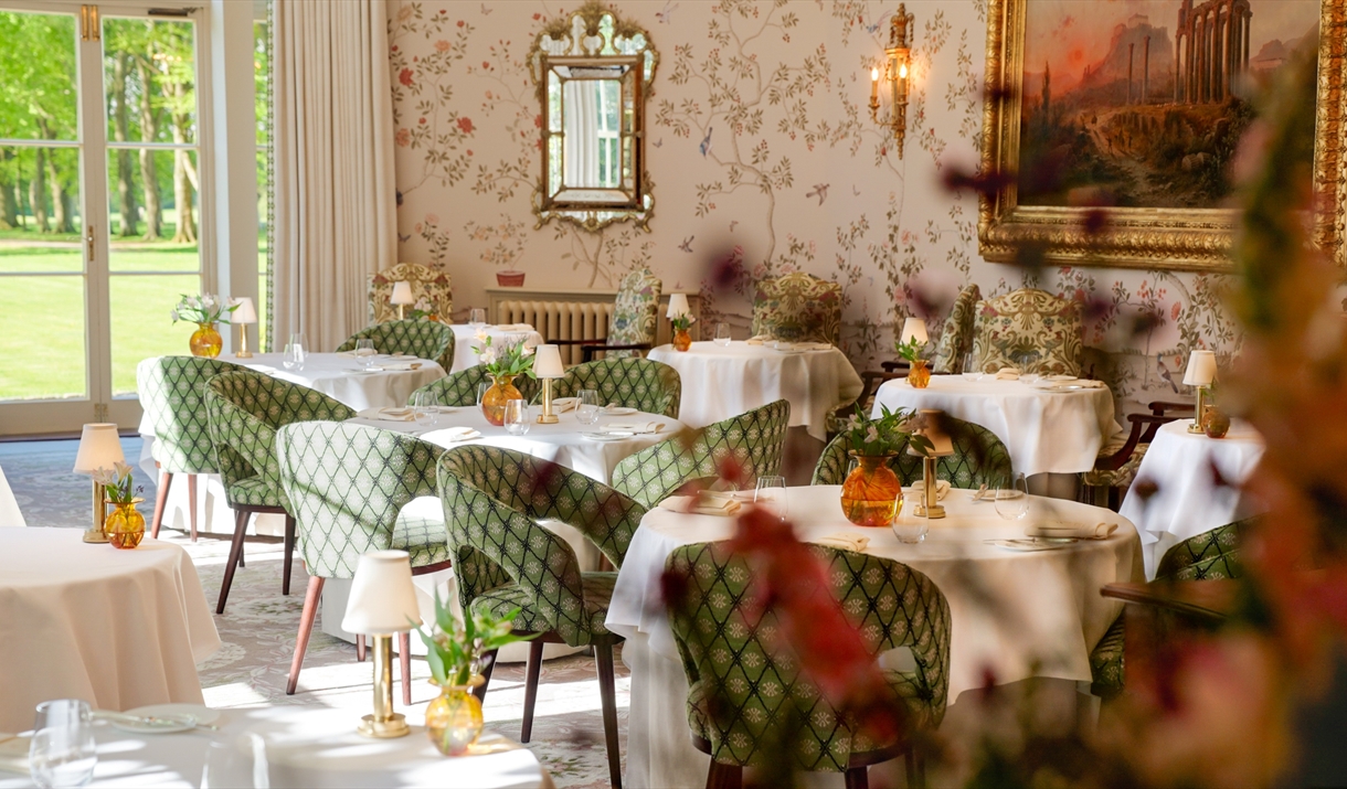 Ornate dining room with decorative wallpaper and chairs, a gold mirror and gold framed painting on the wall.