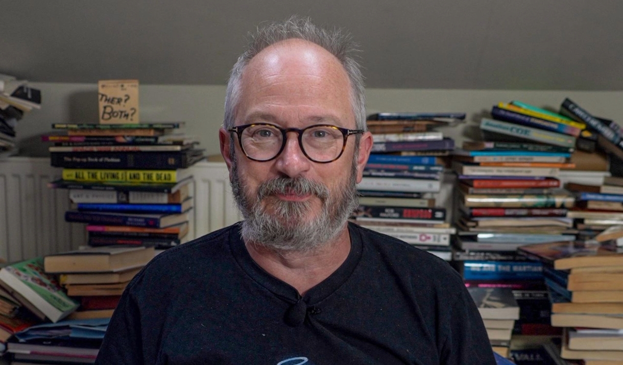 Robin Ince surrounded by stacks of books