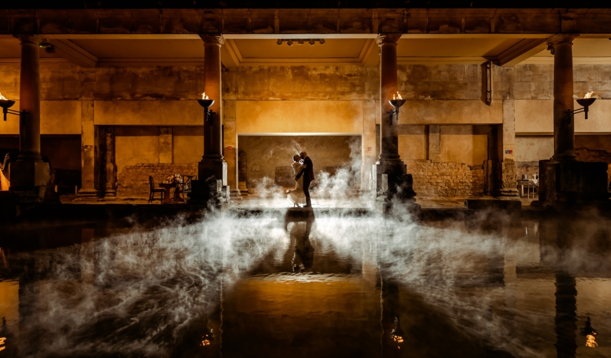 A newly married bride and groom alongside the Great Bath at The Roman Baths in Bath
