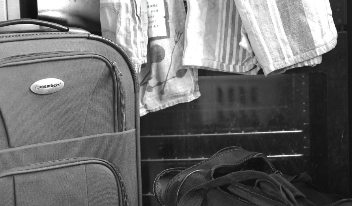 a black and white image shows a suit case and duffle bag in front of a stove with a tea towel across the bar. Sparkfest logo in the top corner