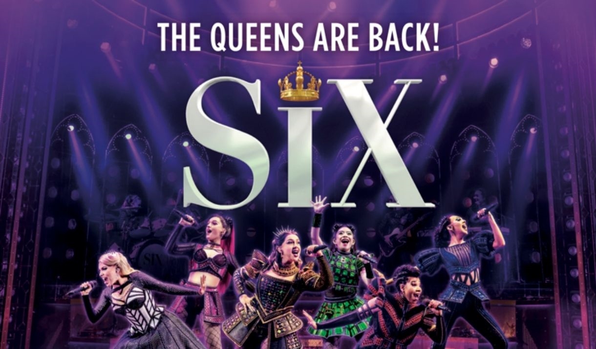 Six performers dressed as modernized versions of Henry VIII's wives are singing and dancing on stage, with the words 'THE QUEENS ARE BACK'.