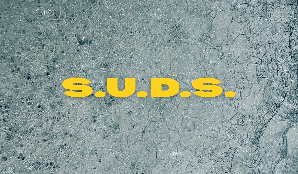 a close up photograph of soap suds with yellow text that reads "S.U.D.S."