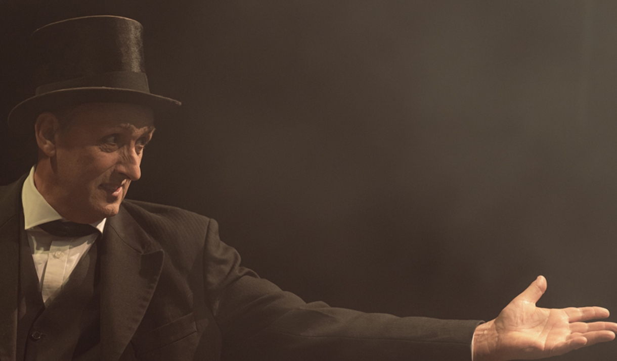 A man in a bowler hat reaches his hand out.